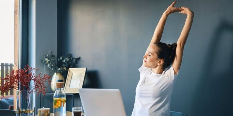 Routine étirements Paris au bureau : femme s'étirant les bras au-dessus de la tête devant son ordinateur portable