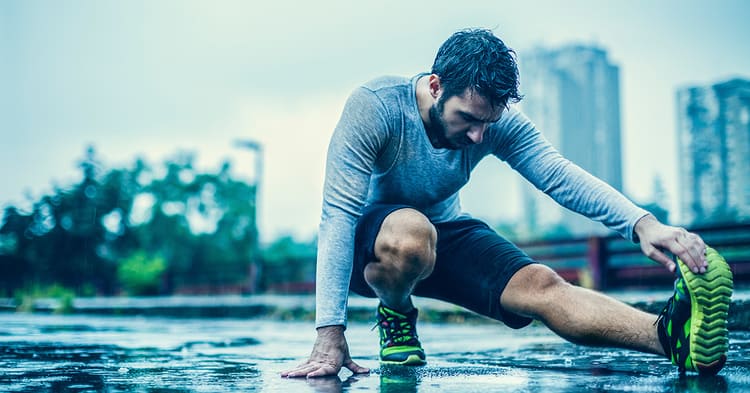 Routine étirements Paris après le sport : coureur s'étirant les ischio-jambiers en extérieur sous la pluie dans un environnement urbain