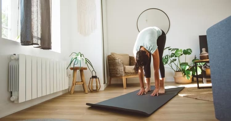 Femme réalisant une flexion avant debout sur tapis de yoga dans un salon lumineux, exercice de souplesse progressive à domicile à Paris