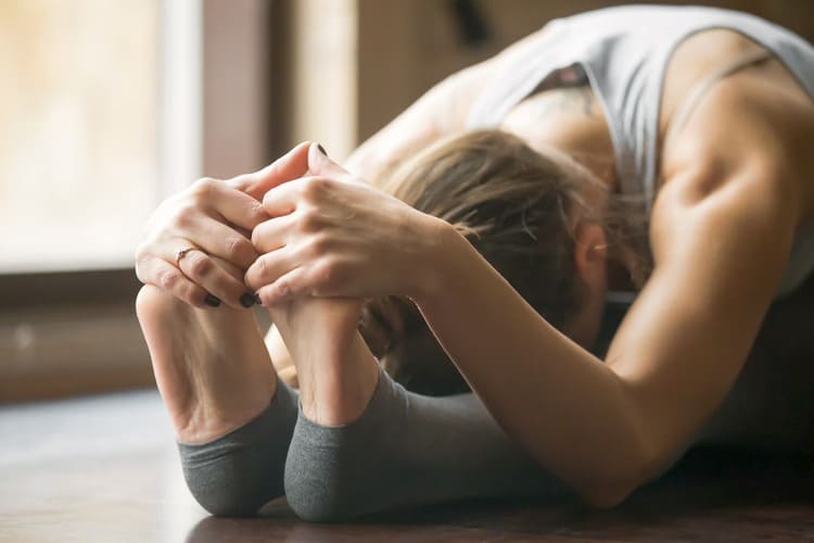 Femme réalisant un étirement passif en flexion avant, tenant ses pieds, illustrant le stretching statique par opposition à la méthode PNF