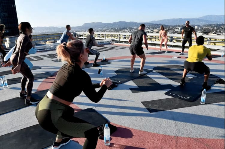 Capital physique : cours de fitness collectif en plein air sur une terrasse urbaine, groupe de sportifs en position de squat et fentes avec vue sur la ville