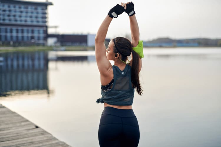 Capital physique : femme sportive s'étirant les bras au-dessus de la tête de dos, au bord de l'eau au lever du jour