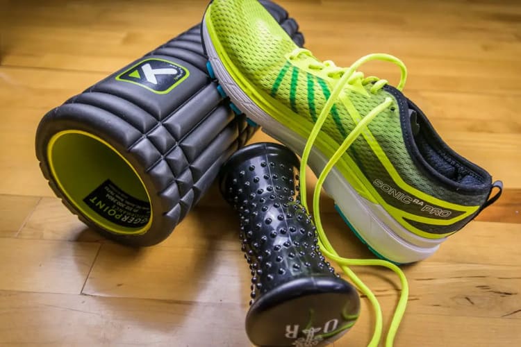 Foam roller texturé et embout de massage à picots, à côté de chaussures de running